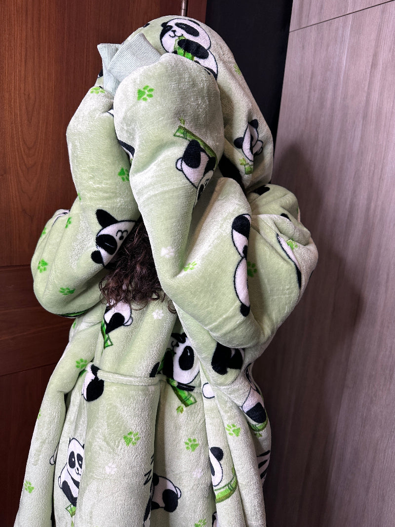 A person wearing a light green Cozify oversized wearable blanket hoodie with a cute panda print covers their face with the hood, showing the soft and plush texture.