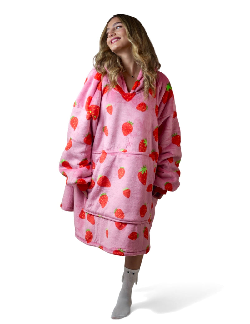 Woman posing playfully in a pink oversized Cozify hoodie blanket with a fun red strawberry print and soft sherpa lining.